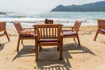 Wooden table and chairs in empty beach cafe next to sea water. Close up, Thailand