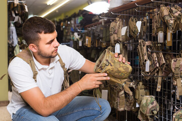 adult man choosing holster for gun in military shop