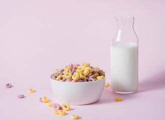 Fototapeta na wymiar sweet colorful cornflakes rings in a white bowl with a bottle of milk on a pink background. Front view and copy space