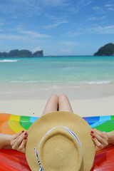 Fototapeta na wymiar Woman wearing a hat and sitting on a inflatable rainbow, viewing to Koh Phi Phi island, Thailand