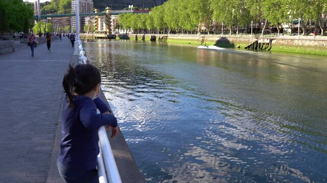 Fast jet ski riding on Bilbao river as little girl observes standing on hand rail. Recreational water sport in the city on sunny day