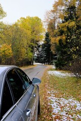 Autumn travel and trips.Road view.First snow. Travel by car. Car on the autumn road.Silver color car on the road with autumn bright trees . Late fall season.