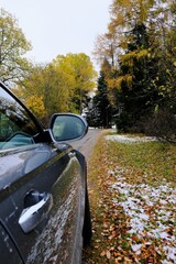 Autumn travel and trips.Road view.First snow. Travel by car. Car on the autumn road.Silver color car on the road with autumn bright trees and the first snow. Late fall season.