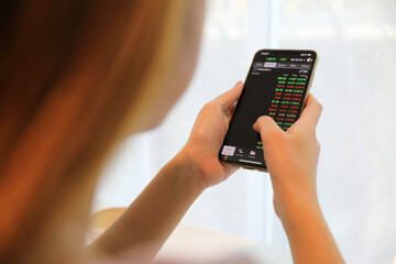 Female hand with smartphone trading stock online in coffee shop , Business concept