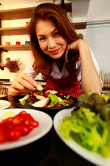 Closeup shot of houswife hand decorating chicken breast green mixed vegetable salad with boiled egg yolk on countertop desk in kitchen with raw fresh organic material in blurred foreground