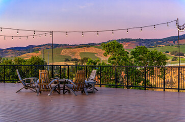 Outdoor al fresco chairs and table on a wooden deck at sunset in the spring with grape vines and hills in the background, Napa Valley, California USA