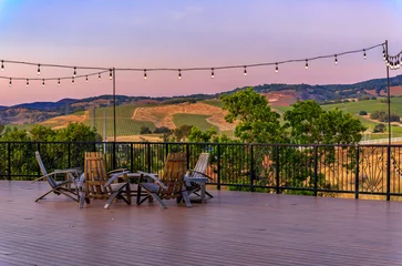 Foto auf Acrylglas Lila Outdoor al fresco chairs and table on a wooden deck at sunset in the spring with grape vines and hills in the background, Napa Valley, California USA