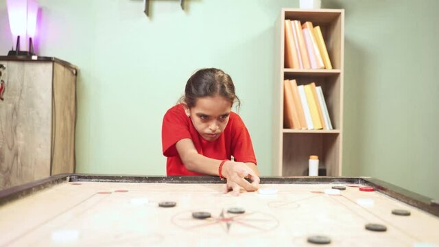 Front view of alone Young girl kid practicing or playing Carrom board at home - Concept of autism and introvert