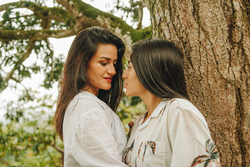 Fototapeta premium Pareja de jóvenes lesbianas se miran entre si mismas al lado de un árbol en la selva peruana. 
