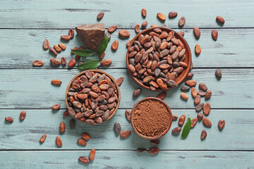 Bowls with cocoa beans and powder on color wooden background