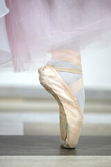 Close up view of beige pointe shoes on tip toes on wooden floor at ballet studio