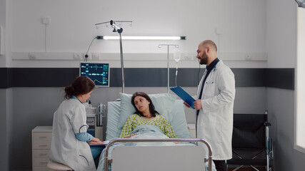 Obraz premium Specialist doctors monitoring sick woman discussing sickness treatment while working in hospital ward. Patient resting in bed explaining symptom disease during recovery appointment