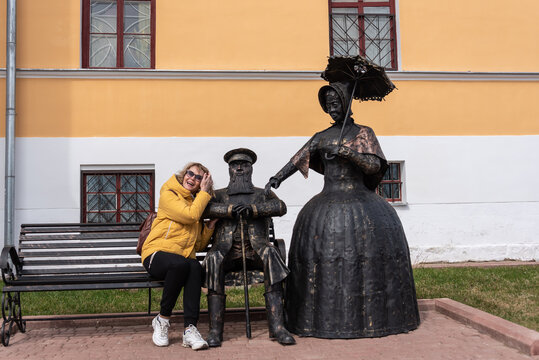 Woman tourist on a bench next to bronze statues in clothes of the last century.