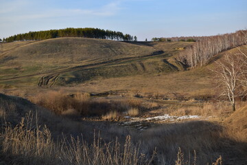 Beautiful landscape in early spring. View of hilly terrain, trees, country road and stream.