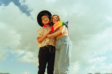 Amigos queer y bisexual abrazándose con la bandera LGTBQ con el fondo de cielo detrás 