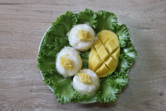 Yellow ripe mango Sheathed and made artistic patterns There is sticky rice topped with sweet coconut milk. Placed on top of green vegetables It is a favorite dessert of Thai people. background is wood