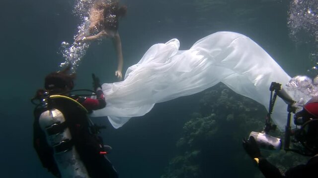 Birth of an angel in creation of underwater model freediver. Creativity and art of creating images on background of seabed. Young woman in white cloth.
