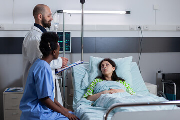Patient with nasal oxygen tube discussing with medical doctors while resting in bed during disease...