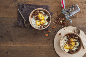 Oatmeal with pineapple, banana and chocolate granola in beige plates on a brown wooden table. A hearty healthy breakfast. A place for text.