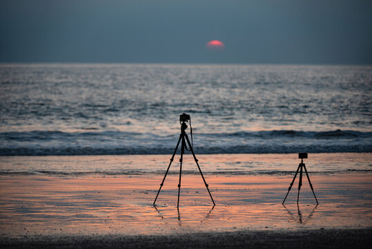 Timelapse on stand. Camera on tripod shooting time lapse panorama on sea at sunset beach.