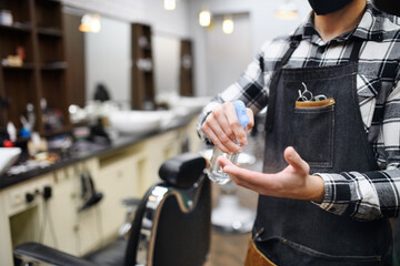 Unrecognizable man haidresser disinfecting hands in barber shop, coronavirus and new normal concept.