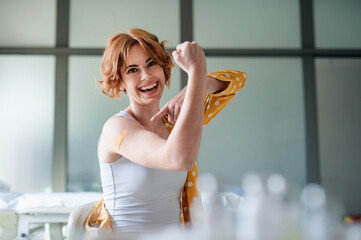Happy young woman with plaster on arm after vaccination in hospital, looking at camera.