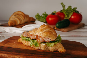 Fresh croissant with ham and lettuce leaves on a light wooden background