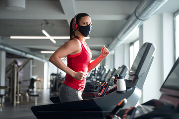 Woman with face mask doing exercise on treadmill in gym, coronavirus concept.
