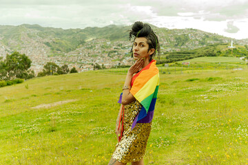 Mujer transgenero parada en el campo sosteniendo bandera LGTBQ en sus hombros  - obrazy, fototapety, plakaty
