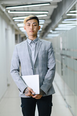 Fototapeta premium business men from Asia in the office. A young Asian manager stands in the office and holds a laptop in his hands