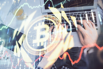 Double exposure of man's hands typing over computer keyboard and crypto currency theme hologram...