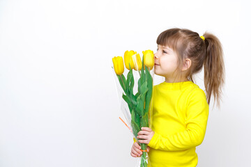 cute baby girl in yellow clothes sniffs yellow flowers on gray background