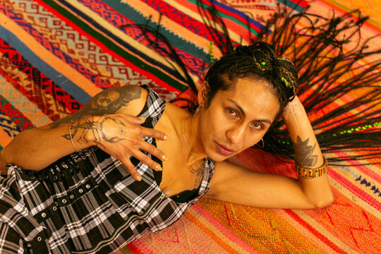 Mujer transgenero con trenzas acostada sobre alfombra andina 