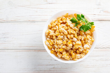 Frozen corn in a plate on white table. Frozen food. Top view. Copy space