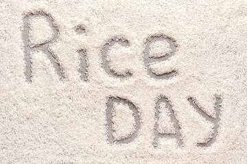 Text RICE DAY on white basmati rice background. Celebration of national paddy day. Or concept of healthy food for vegan diet. Top view