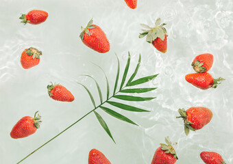Natural summer fruits texture made of tropical palm leaf and red strawberris float on the water on the pastel green background. Raw food refreshment concept. Minimal flat lay.