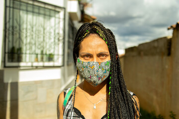 Retrato frontal de mujer transgénero con trenzas usando mascarilla en la calle 