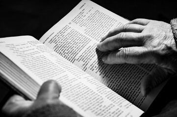 hands of elderly woman pray on bible
