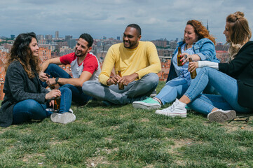 Happy fiends sitting in a park talking, laughing and drinking beer