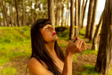 Mujer transgénero madura soplando una flor amarilla en medio del bosque 
