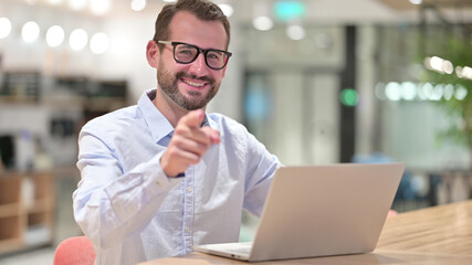 Businessman with Laptop Pointing at the Camera in Office