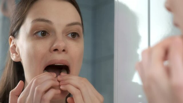 Young woman is installing splint for down teeth to correct the bite looking at mirror in bathroom. Inserting aligners on down teeth for correcting jaw joints. Dentistry treatment.