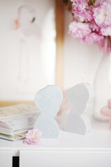 Two grey and blue candles shaped as greek goddess on a white furniture surrounded by pink blossom, close up