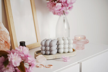 A grey-blue bubble candle on a white surface surrounded by pink cherry blossom