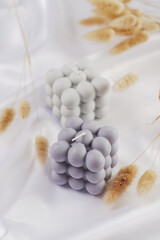 A grey-blue bubble candle on a white silky fabric and yellow wheat branches