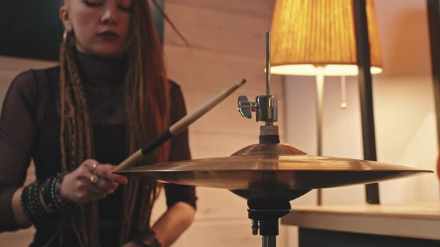 Slowmo closeup of young woman with dreadlocks and gothic makeup holding sticks and playing drums indoors in studio