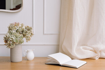 Ceramic vase with dry hydrangea, jug and notebook open at blank page. Comfortable modern interior design.