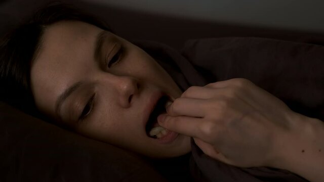 Portrait of young woman is installing her invisible orthodontic aligners for dental correction lying in bed at night. Dentistry and stomatology treatment. Splint for down teeth to correct the bite.