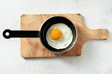 fried egg in a frying pan and on a cutting wooden board