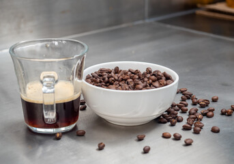 Roasted coffee beans in white bowl with americano in glass cup on table